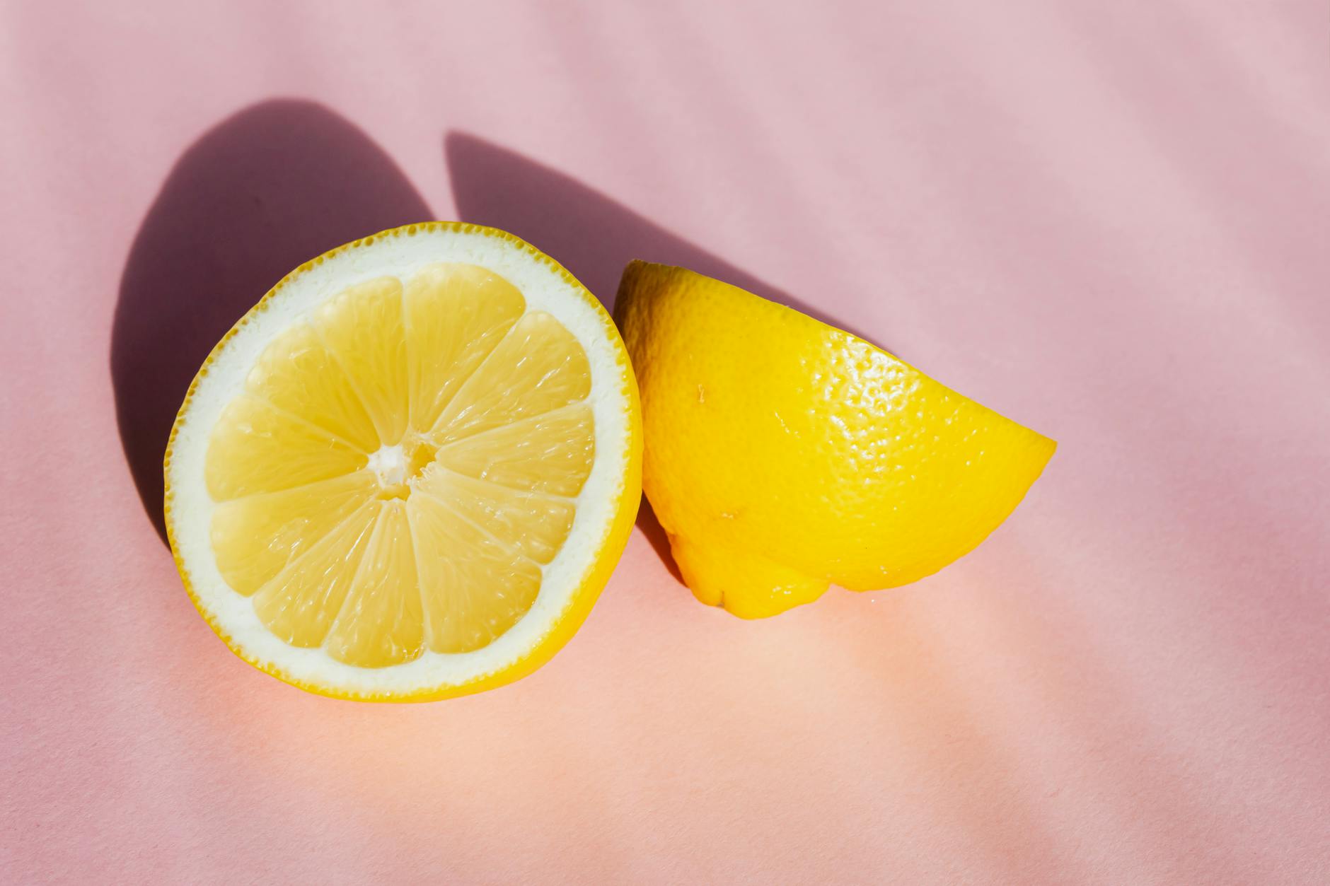 Fresh lemon halves on a pink background with natural sunlight
