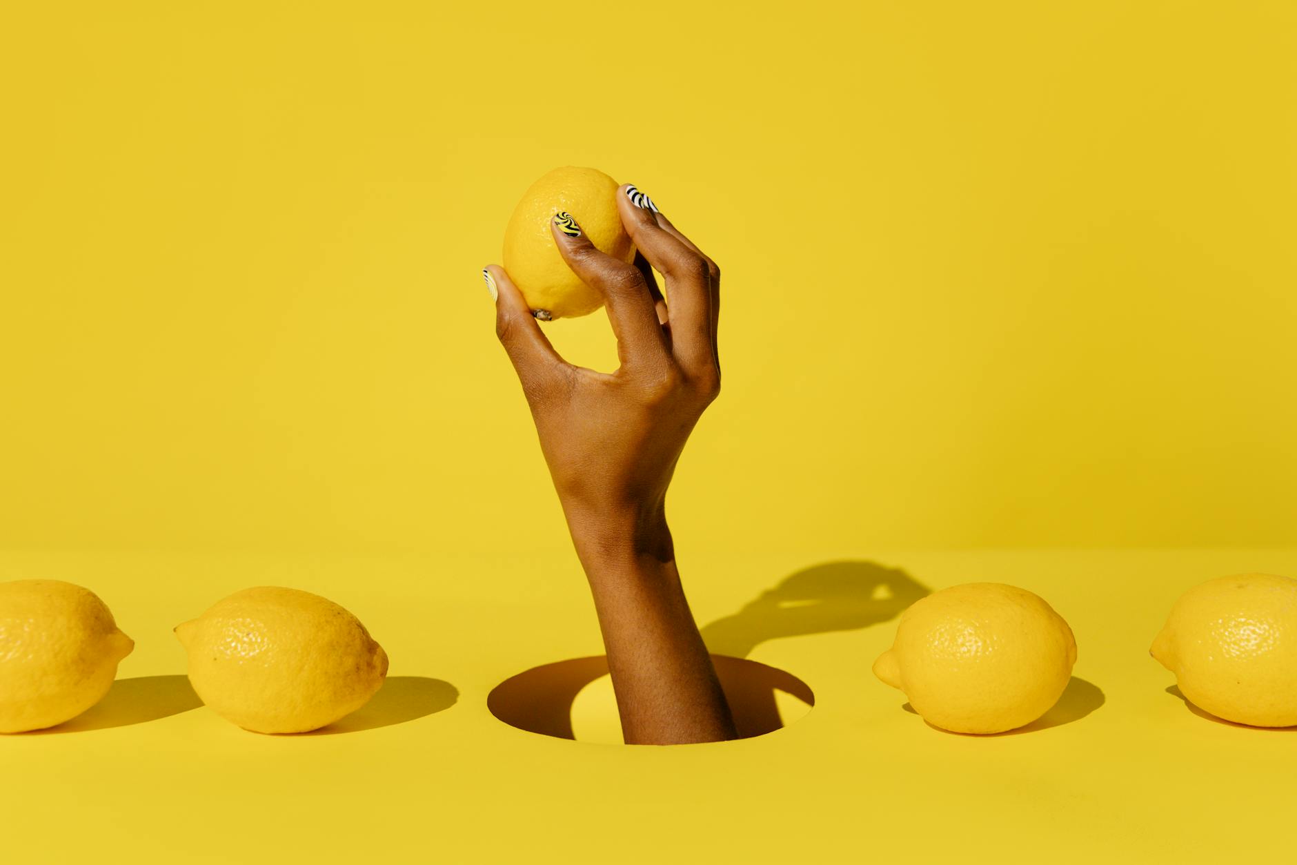 A hand holding a fresh lemon against a vivid yellow background, conveying freshness and citrus appeal