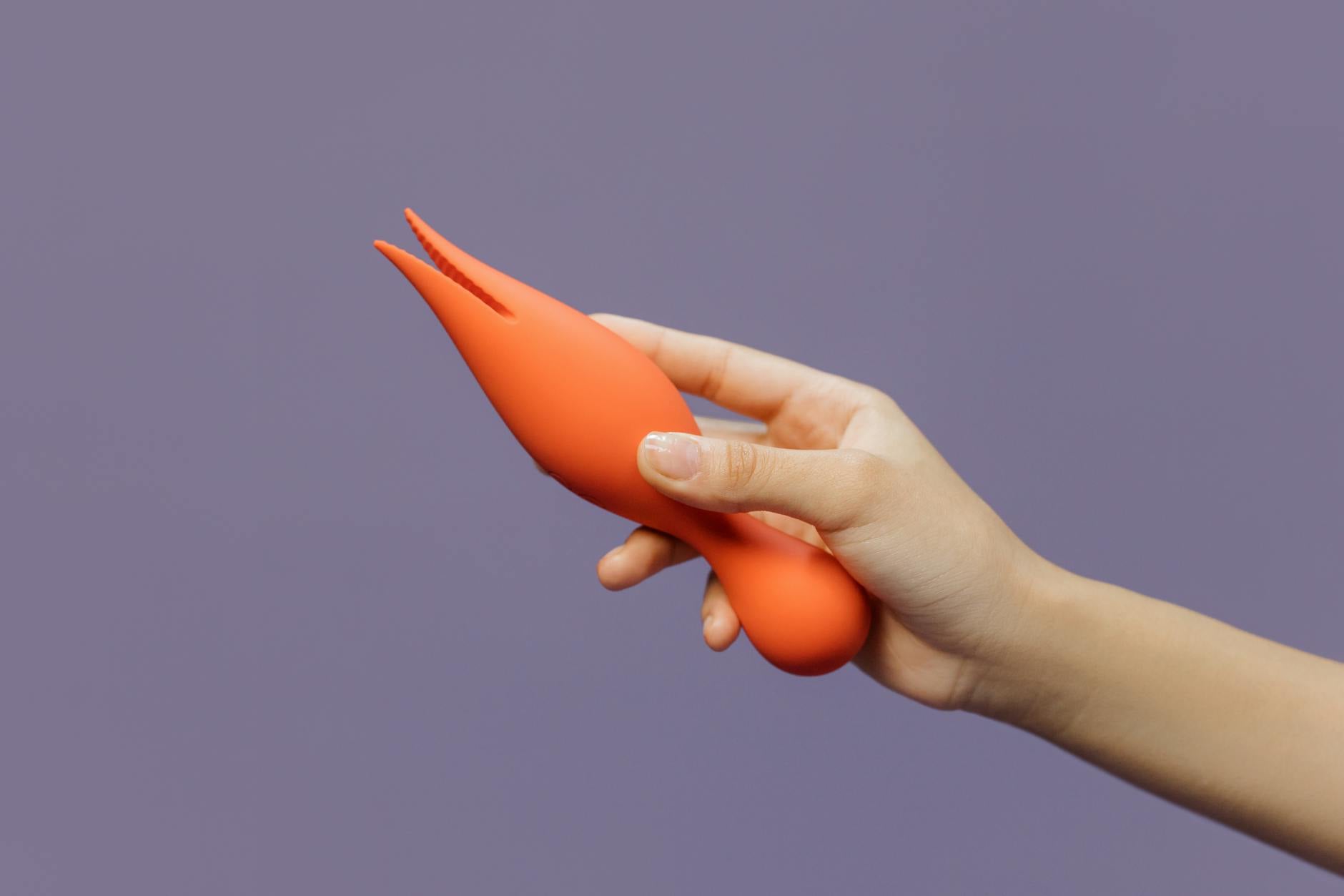 Close-up of a hand holding a yellow lemon vibrator against a minimalistic backdrop, showcasing sensual pleasure tools.