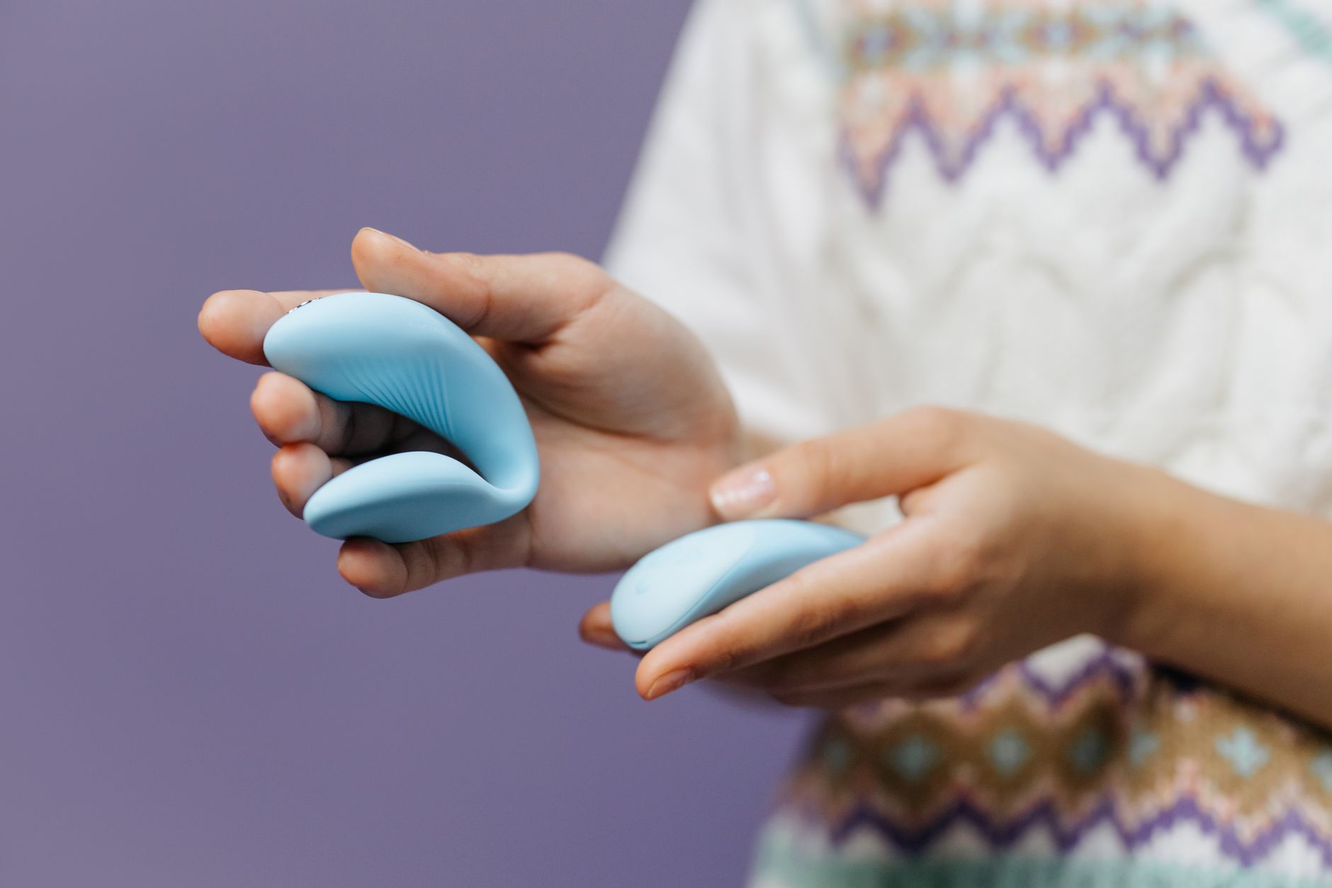 Hand holding a sleek blue lemon vibrator against a soft purple background