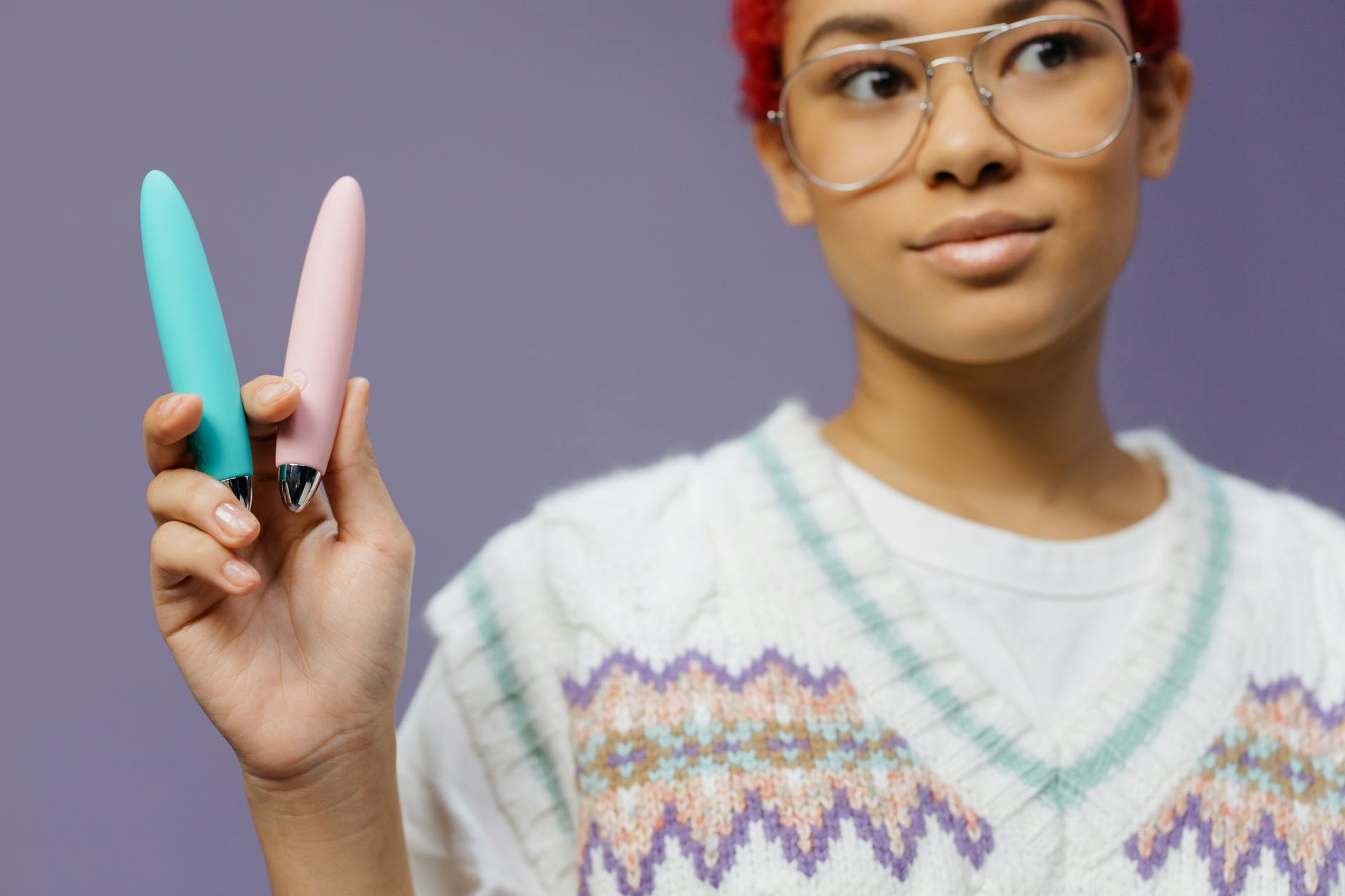Two hands holding pastel-colored silicone sex toys together against a neutral background