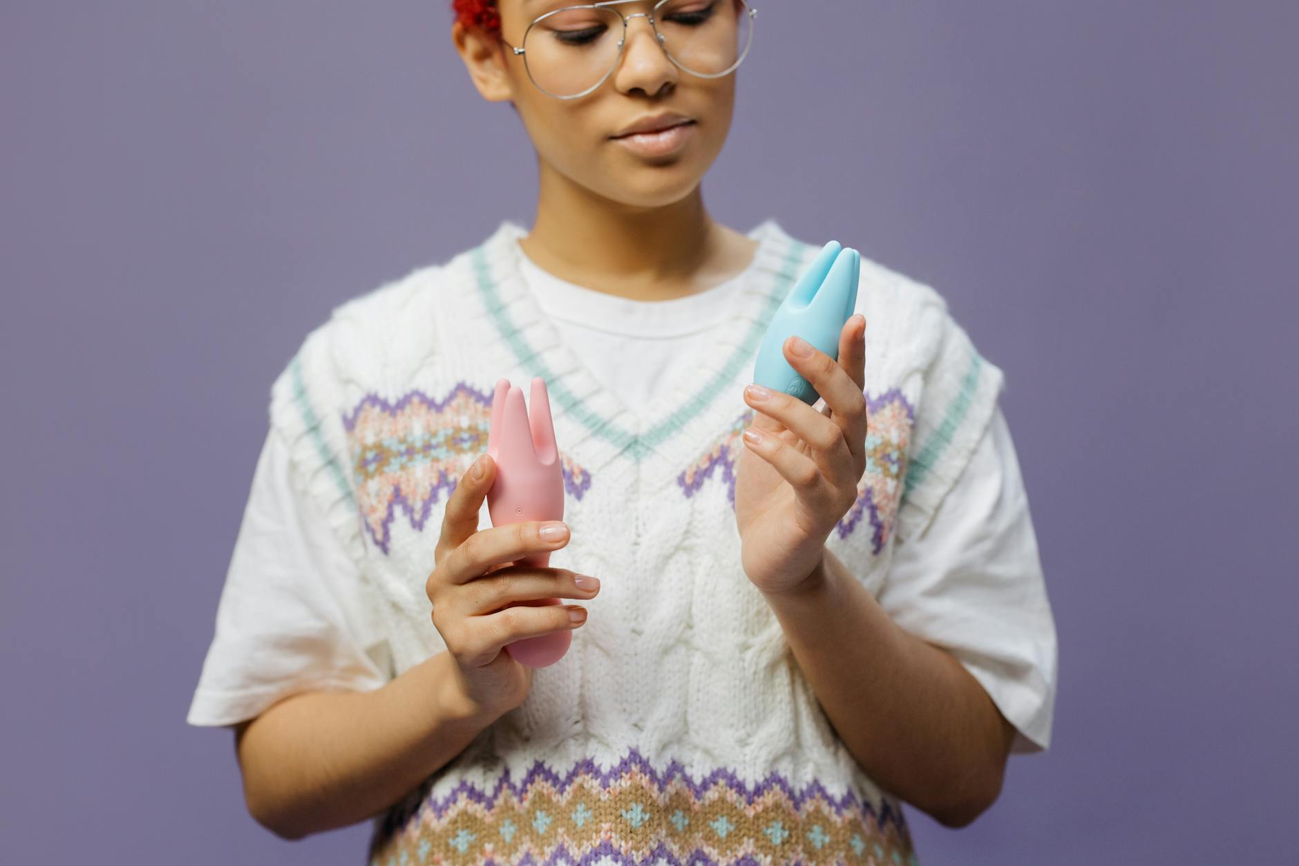 Woman holding blue and pink silicone vibrators contemplatively
